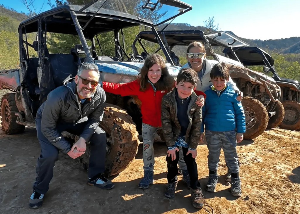 Family of five posing beside six-seat UTVs after an off-road ride
