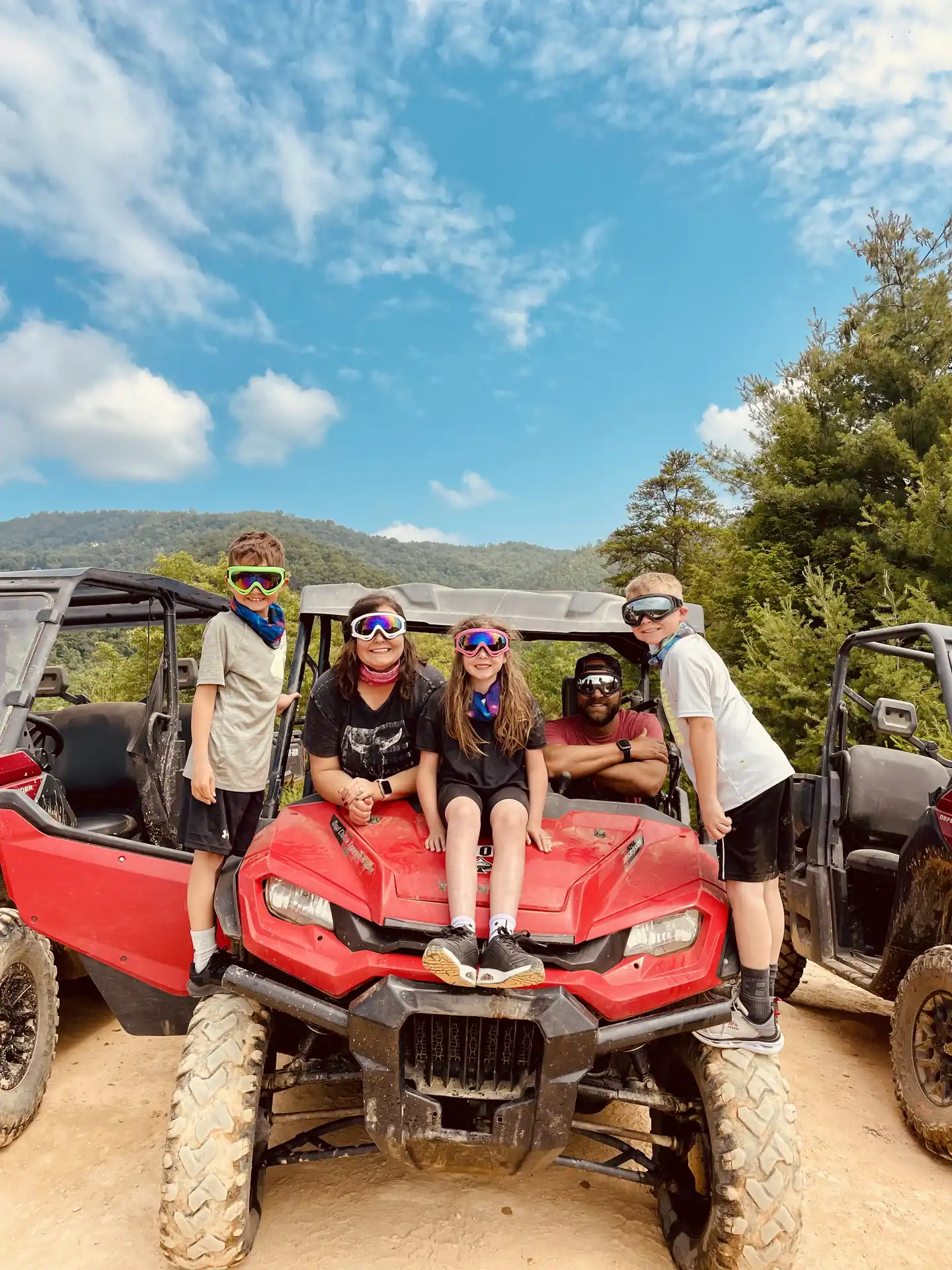 Family wearing goggles poses on an ATV with mountain views