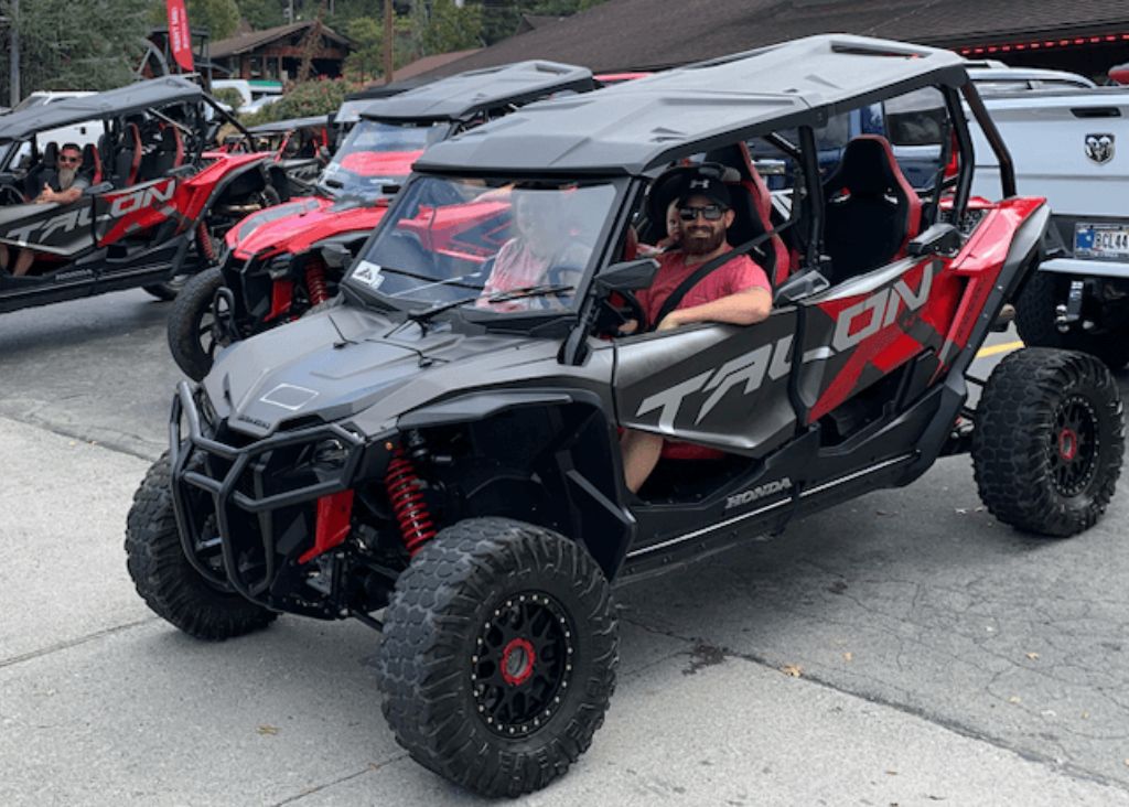 People in a 4 door red Honda Talon UTV rental getting ready to explore the mountains